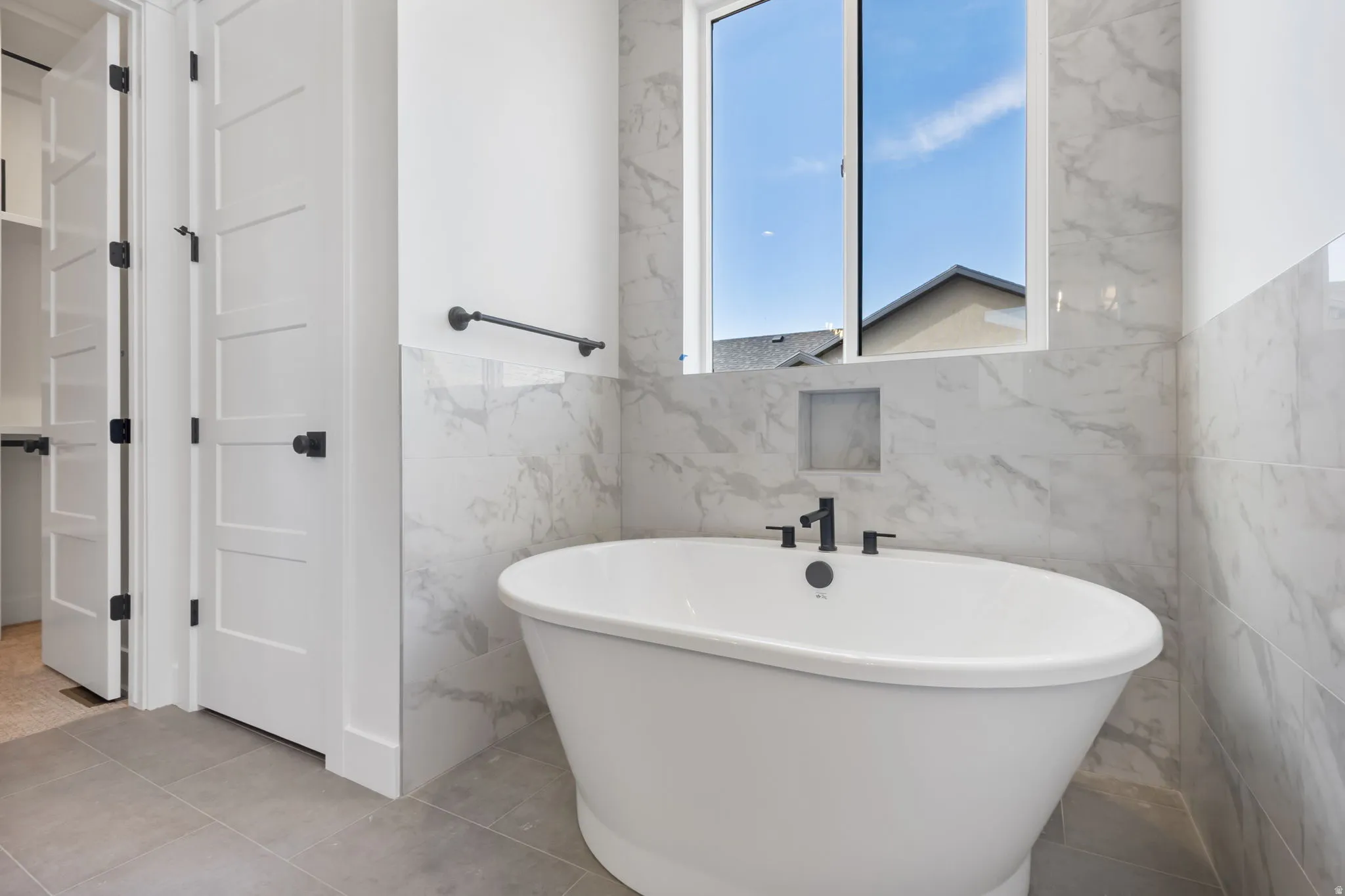 Freestanding soaking tub with matte black fixtures, set against large format marble-look wall tiles