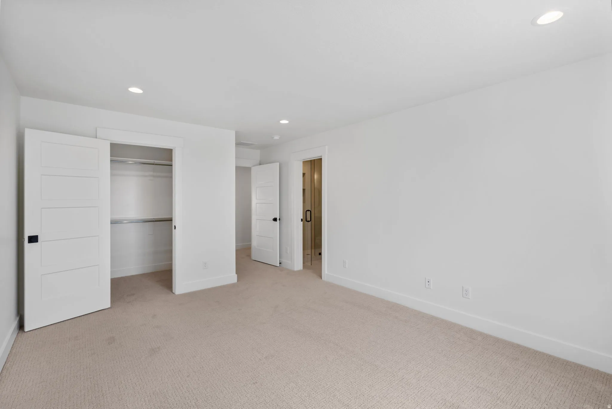 Spacious room featuring neutral carpeting, white walls, recessed ceiling lighting, and a closet with bifold doors