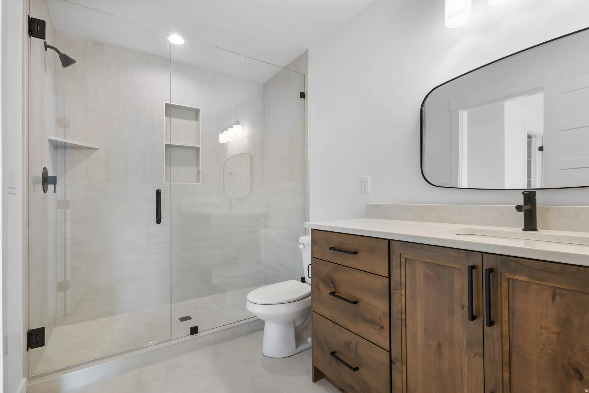 Modern bathroom featuring a frameless glass shower enclosure with matte black fixtures, a built-in shower niche, and a corner shelf