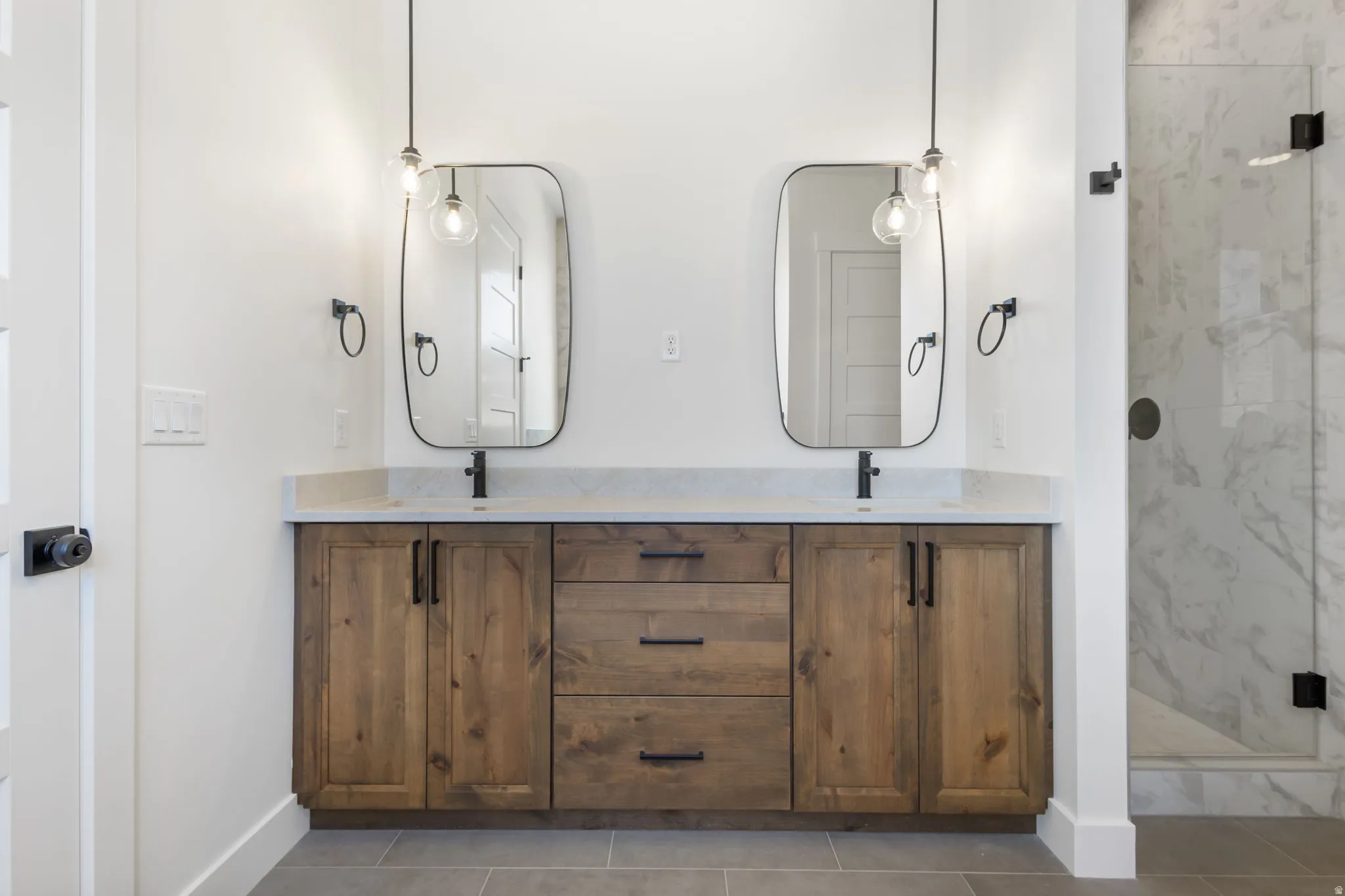 Dual wood-finish vanities with light stone countertops, integrated sinks, and matte black hardware
