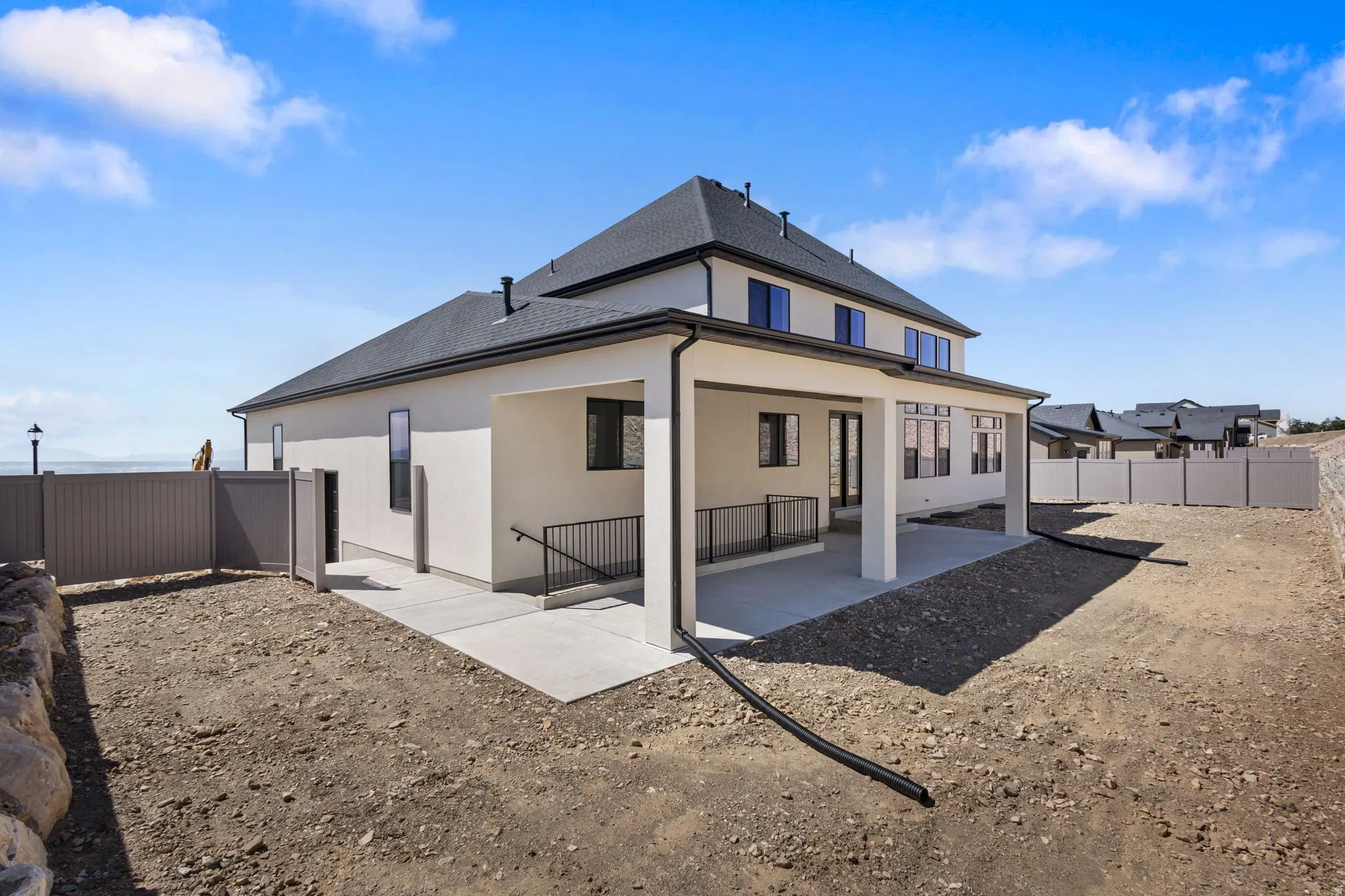 Contemporary stucco exterior with a covered patio featuring a concrete slab and black railing