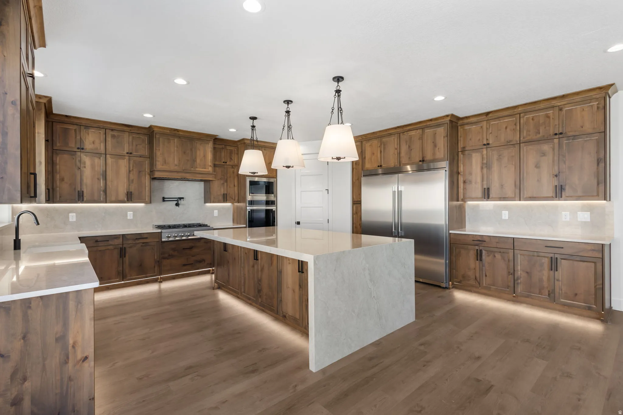 Gourmet kitchen featuring a large central island with pendant lighting, wood-finish cabinetry, stainless steel appliances, and wood-finish flooring