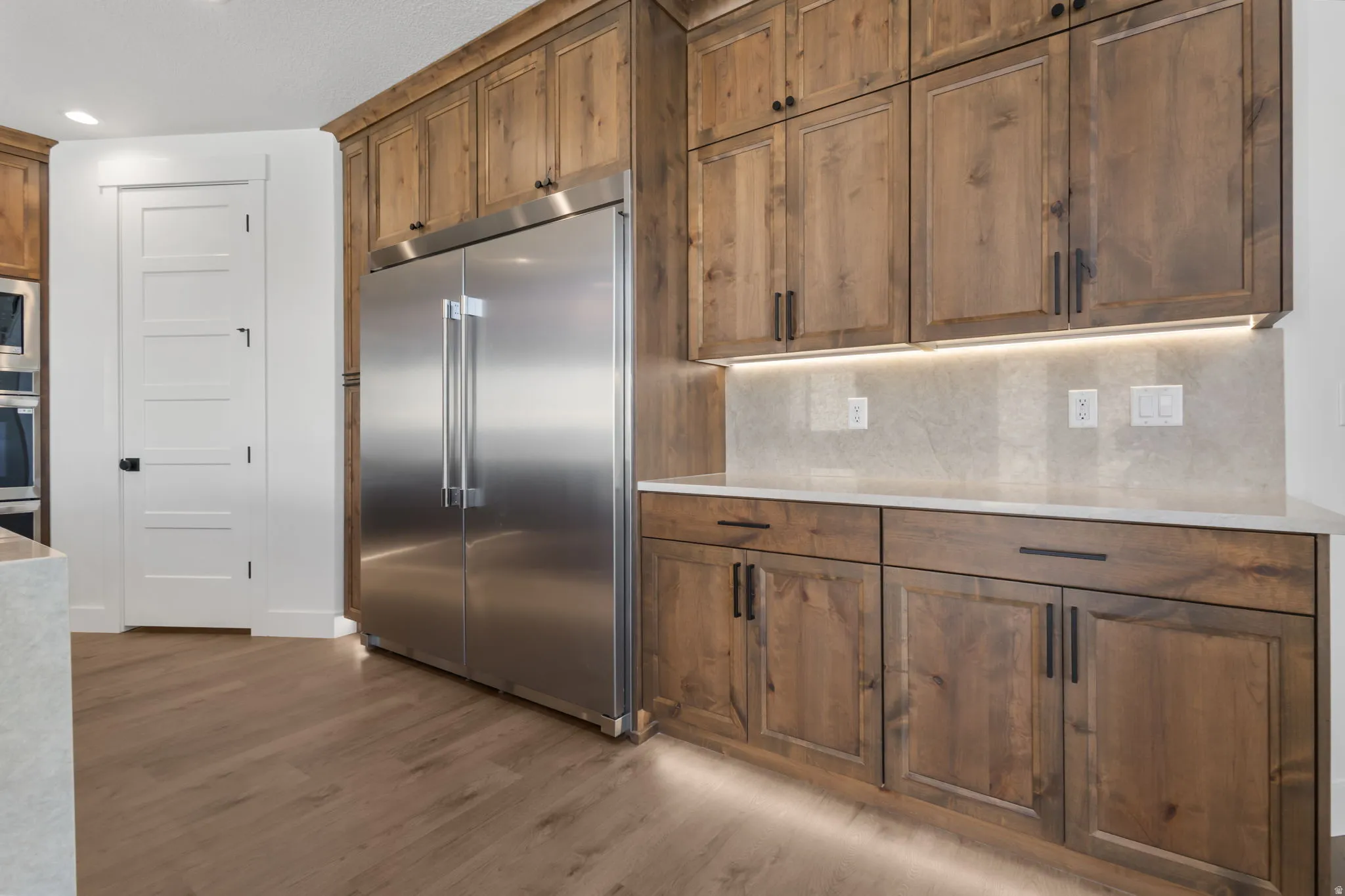 Spacious kitchen featuring floor-to-ceiling wood cabinetry, a stainless steel side-by-side refrigerator, white countertops, and wood-finish flooring