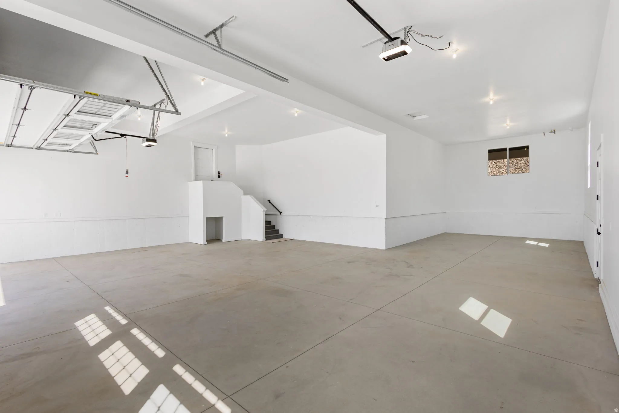 Spacious garage featuring a concrete floor, bright white walls with wainscoting, and recessed lighting