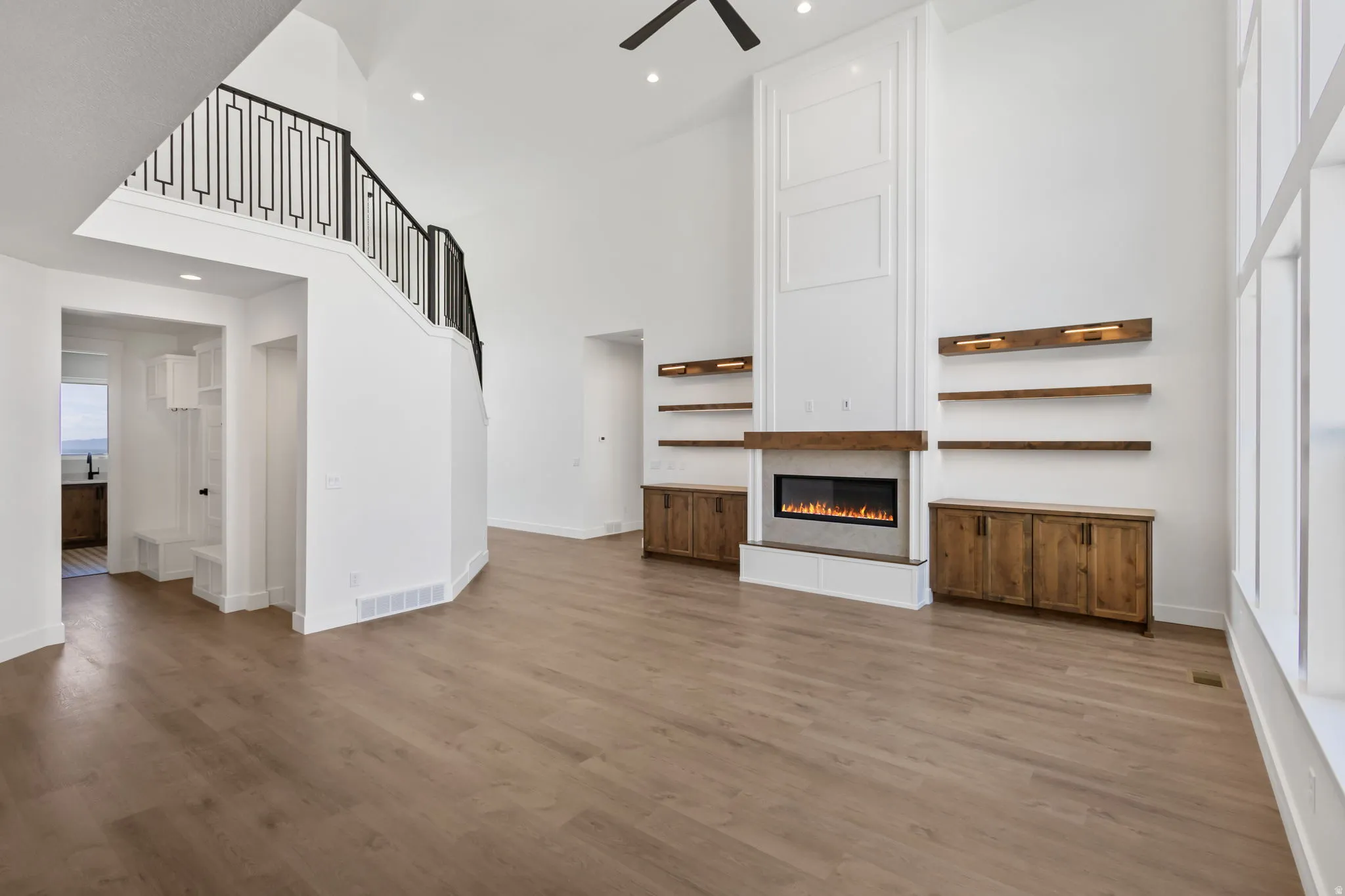 Great room featuring a tall vaulted ceiling, wood-finish flooring, a contemporary fireplace with a wood mantle, custom built-in cabinetry, and a striking staircase with decorative metal railing