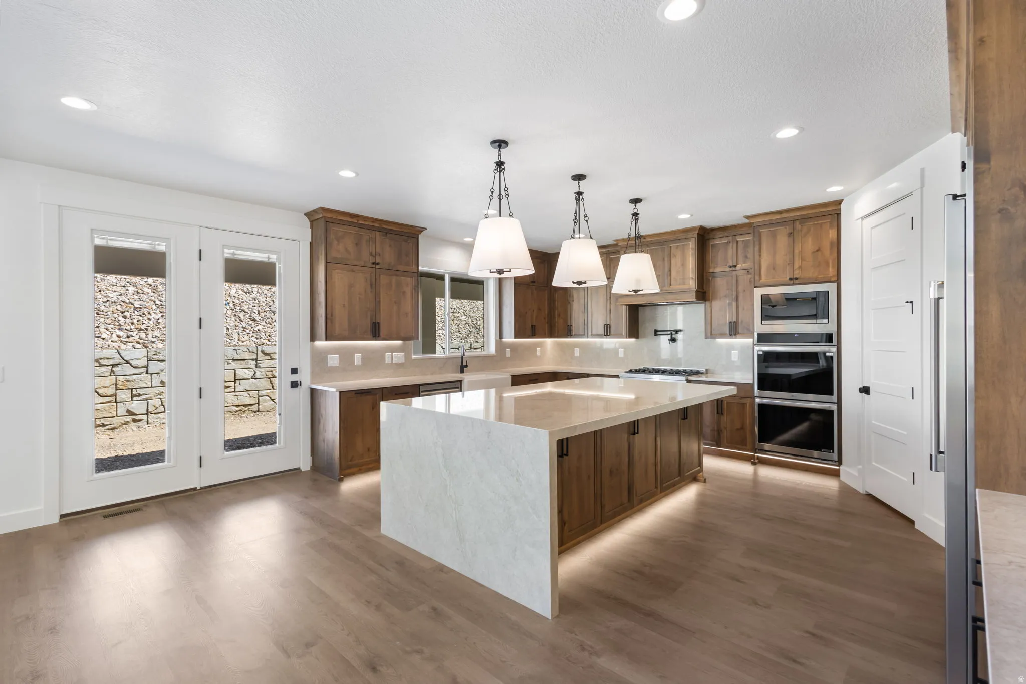 Spacious kitchen featuring an oversized island with waterfall countertop, recessed lighting, and wood-finish flooring
