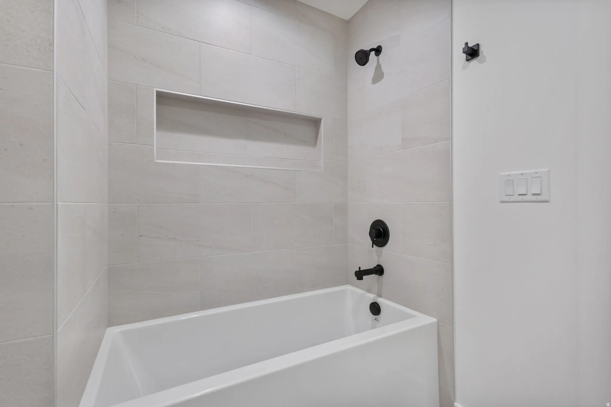Bathtub with matte black fixtures, light-toned wall tiling, and an integrated shower niche