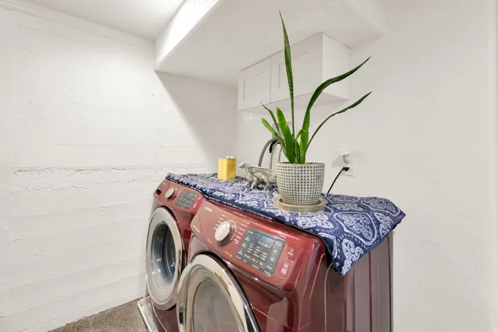 Dedicated laundry area featuring a front-load washer and dryer set, white overhead cabinetry, and textured white walls