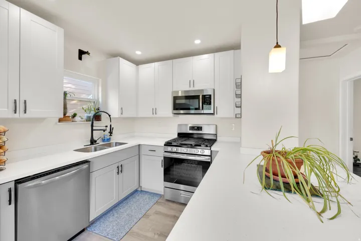 Kitchen featuring white upper cabinetry, gray lower cabinetry, stainless steel appliances, a double basin sink with a matte black faucet, and light wood-finish flooring