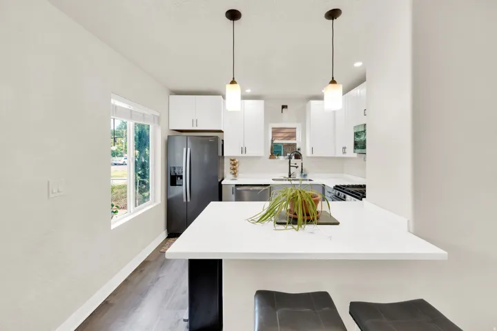 Kitchen featuring white shaker cabinetry, stainless steel appliances, quartz countertops, a kitchen island with seating, and wood-finish flooring
