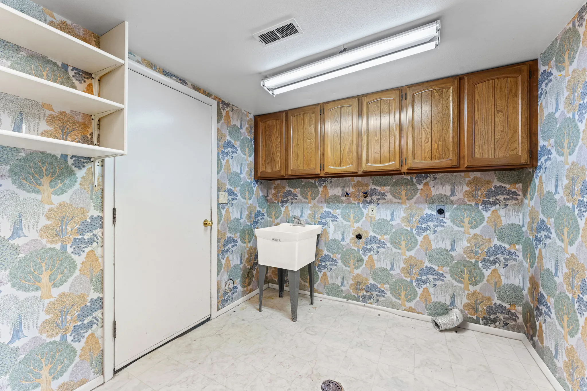 Utility room featuring a utility sink, wood-finish wall cabinetry, open shelving, and a fluorescent ceiling light fixture