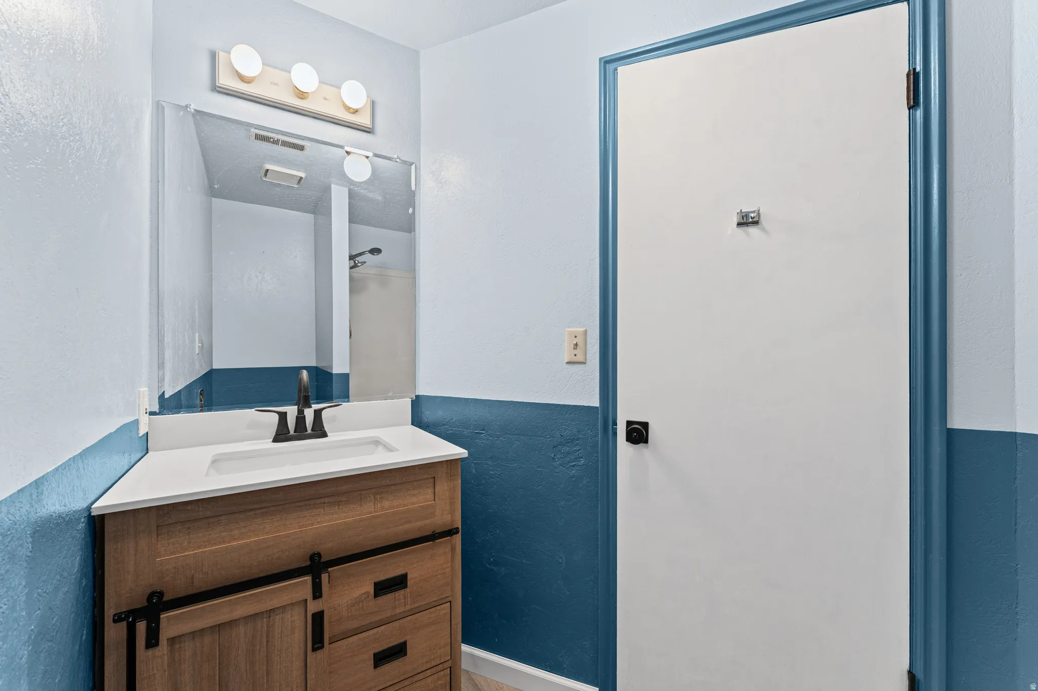 Contemporary vanity featuring a wood-finish cabinet with barn door style accents, a white countertop, and an integrated rectangular sink