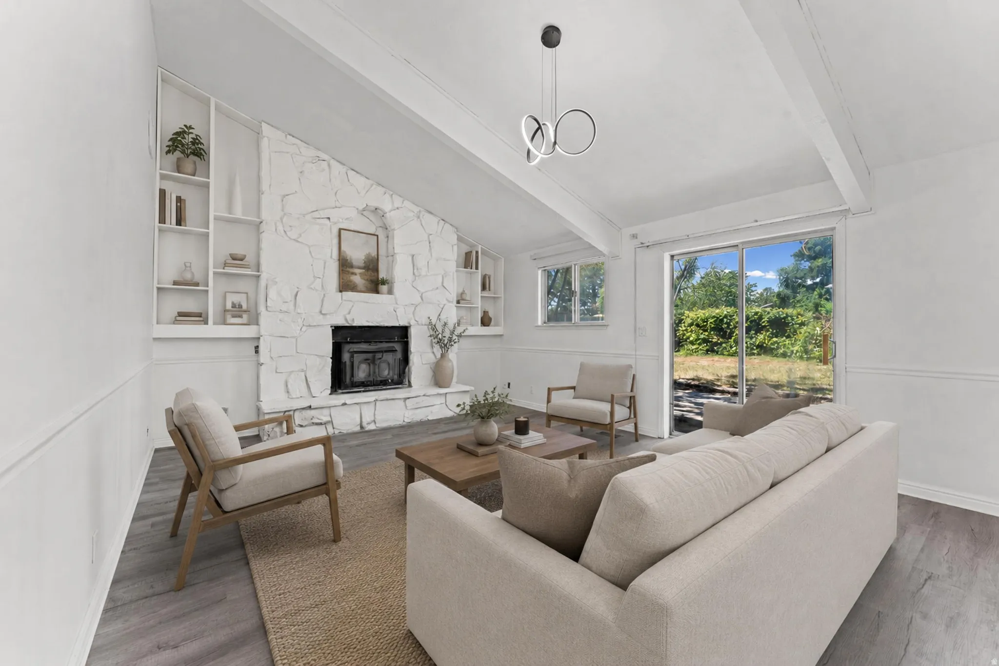 Vaulted ceiling living area featuring a stone-clad fireplace, integrated shelving, wood-finish flooring, and a sliding glass door to the exterior