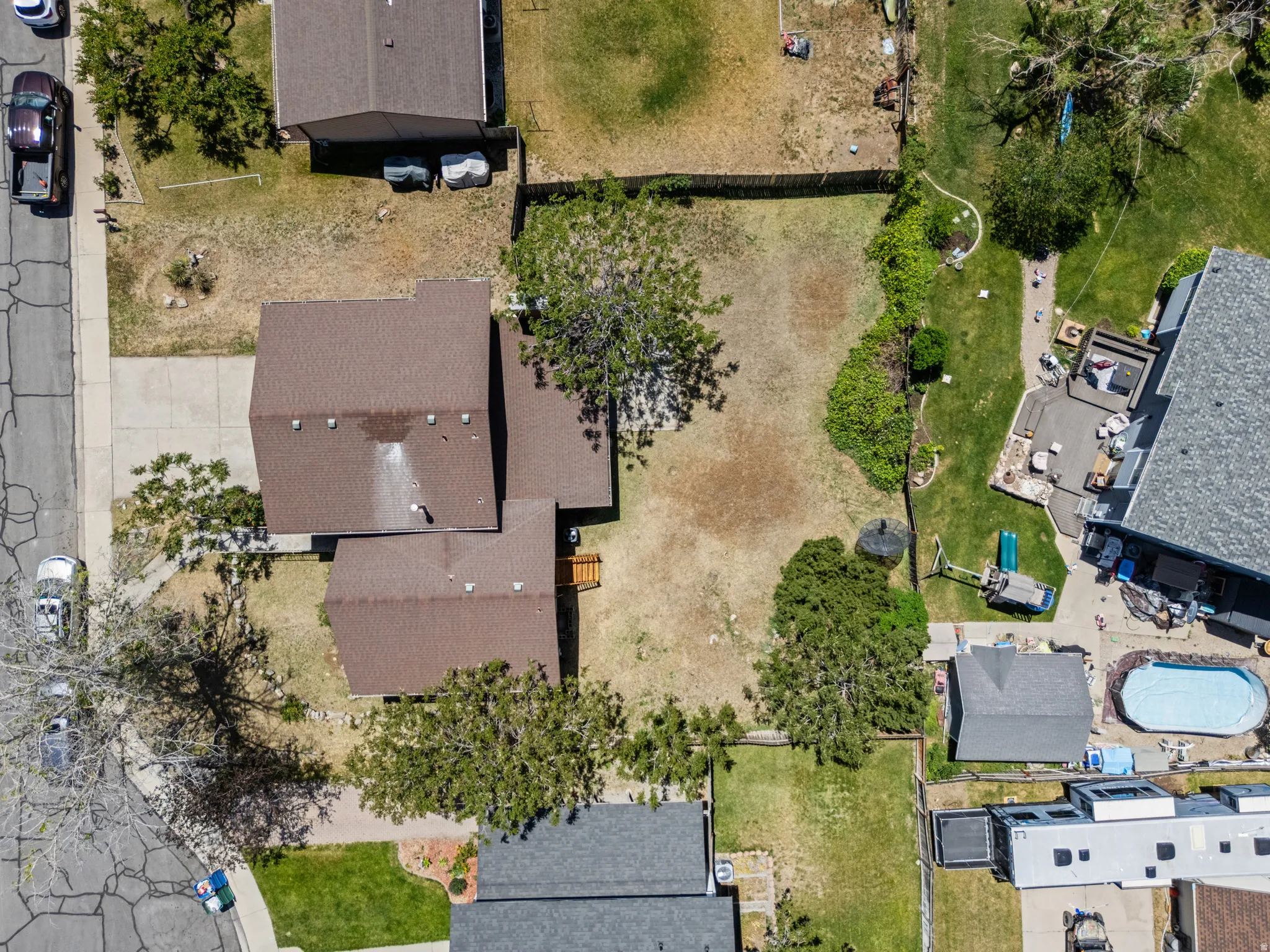 Aerial view showcasing a residential property with a brown-roofed structure, featuring a front driveway and mature trees on the lot