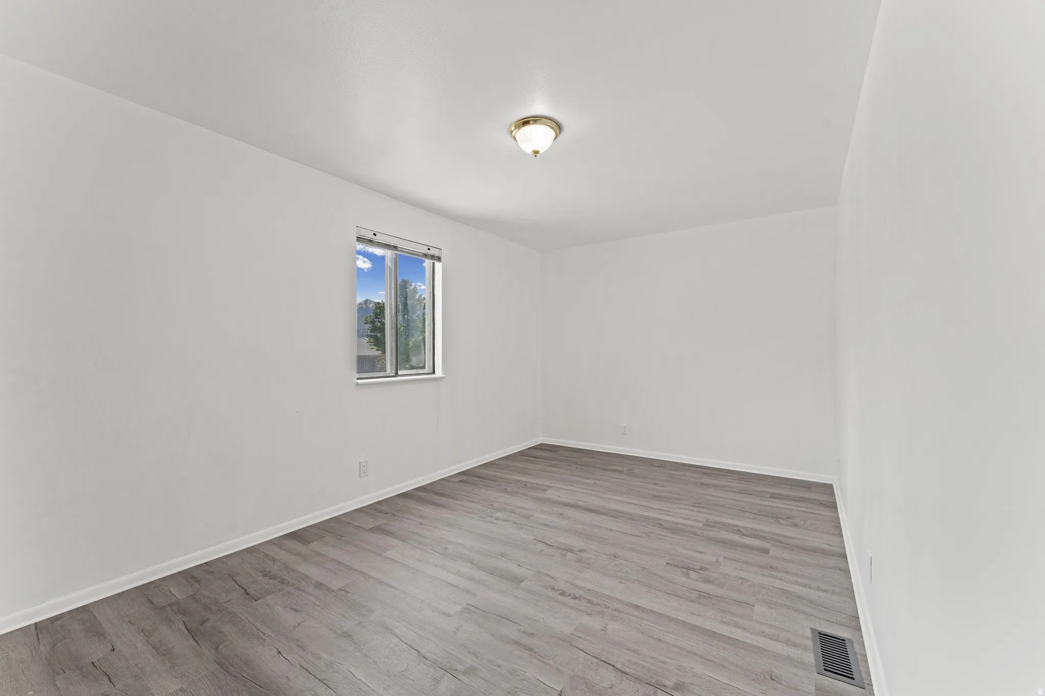 Spacious room featuring light wood-finish flooring, white baseboards, and bright white walls