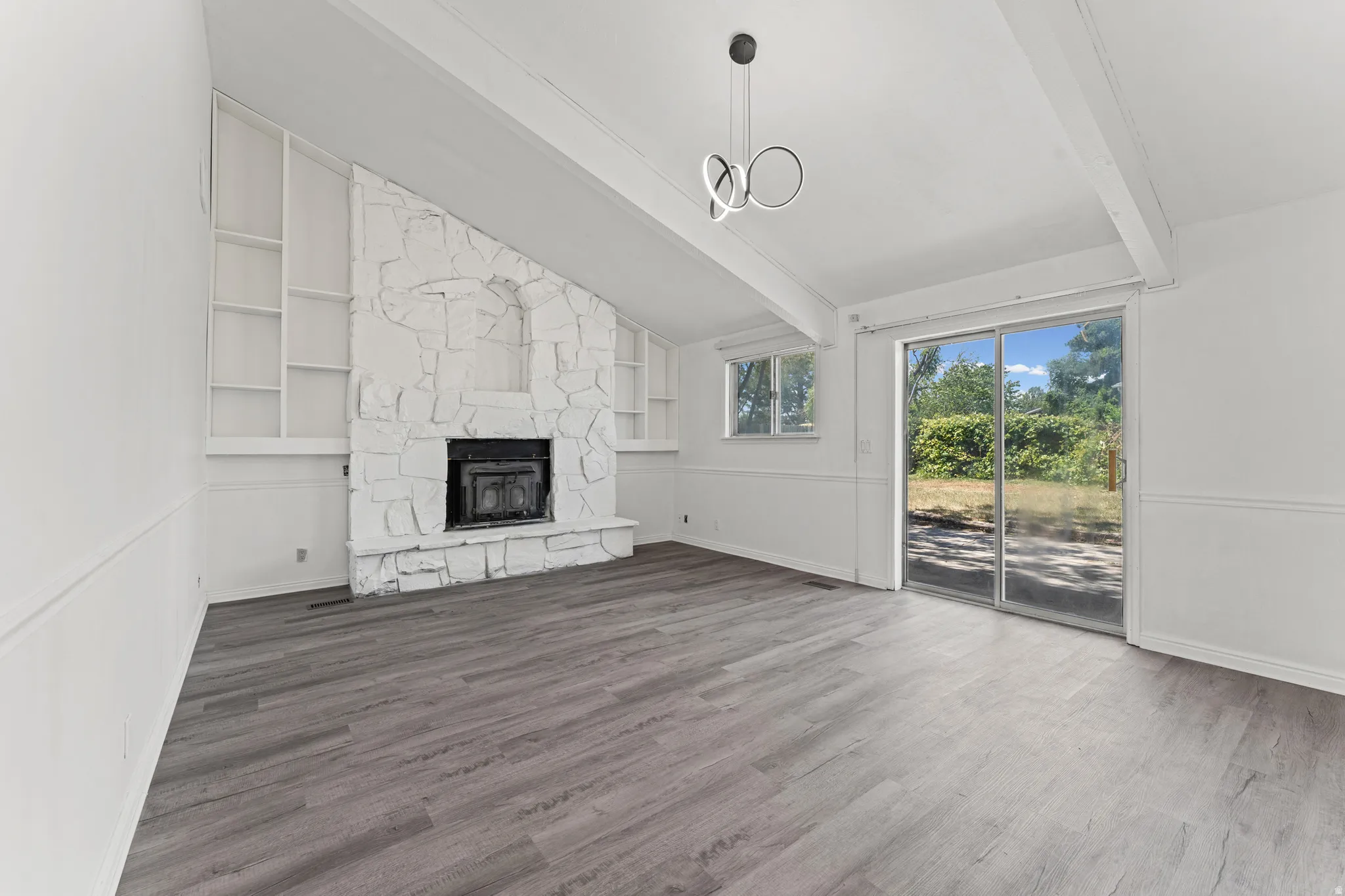 Spacious room featuring wood-finish flooring and a stone fireplace with hearth