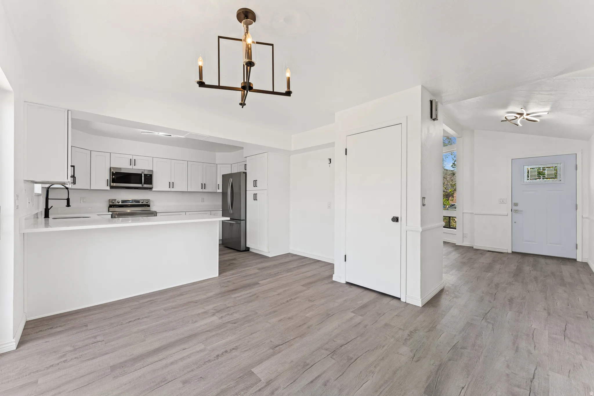 Open concept living space featuring wood-finish flooring, a contemporary chandelier, and a kitchen with white cabinetry, stainless steel appliances, and a breakfast bar