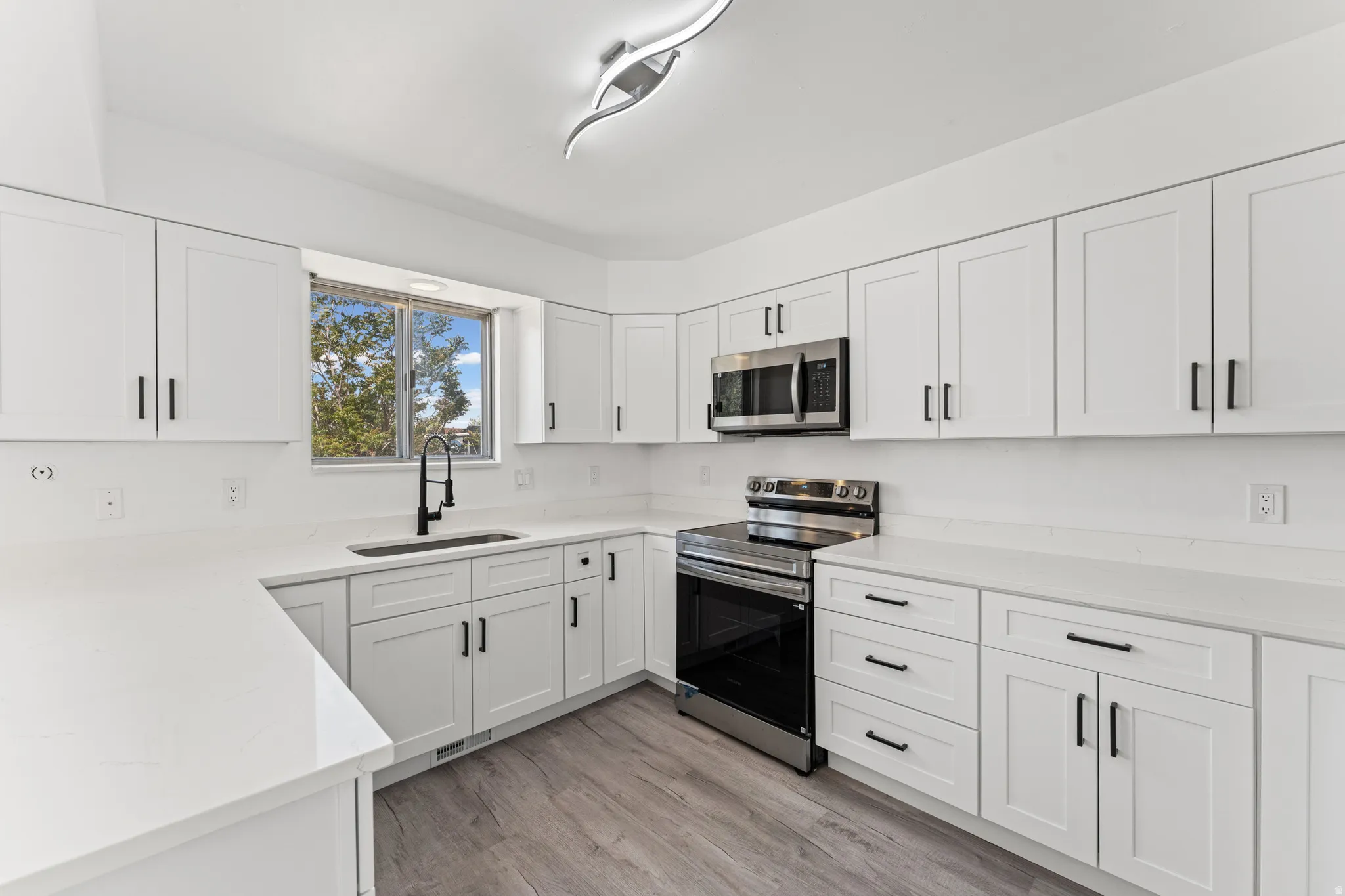 Kitchen featuring white shaker-style cabinetry with matte black hardware, white countertops, and wood-finish flooring