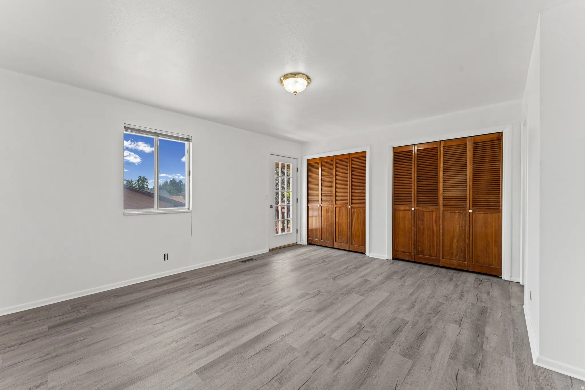 Spacious room featuring light gray wood-finish flooring, white walls, and a window providing natural illumination