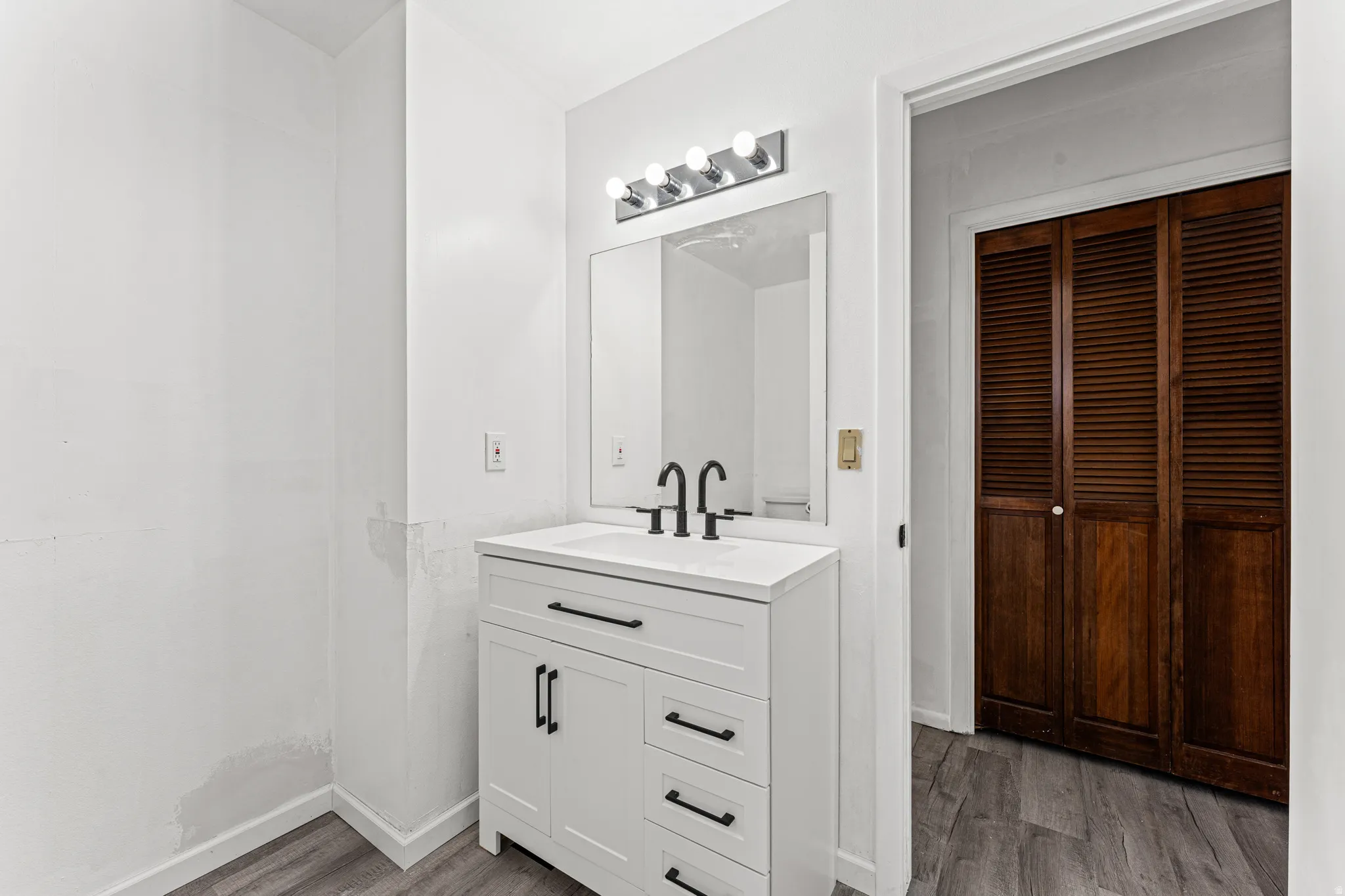 White vanity with a rectangular sink and matte black faucet, illuminated by a four-bulb vanity light fixture