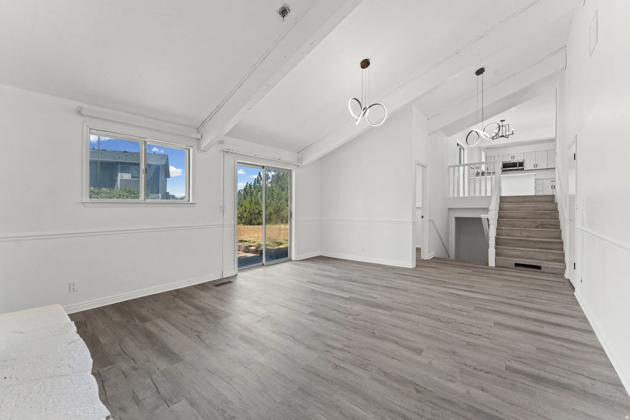 Vaulted ceilings with exposed beams, wood-finish flooring, and white wainscoting