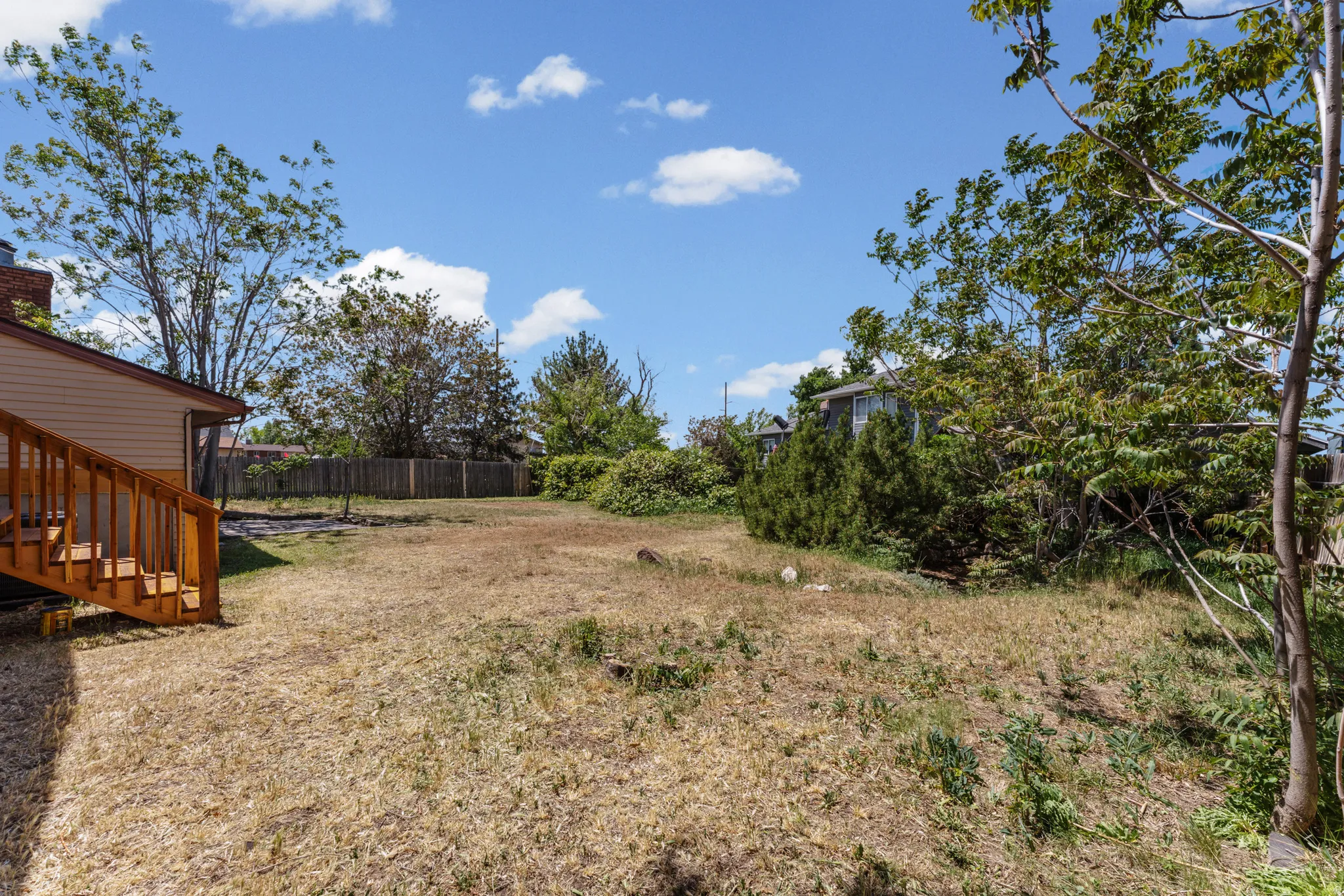 Expansive outdoor space featuring a sloped, grassed area and a wooden deck with stairs