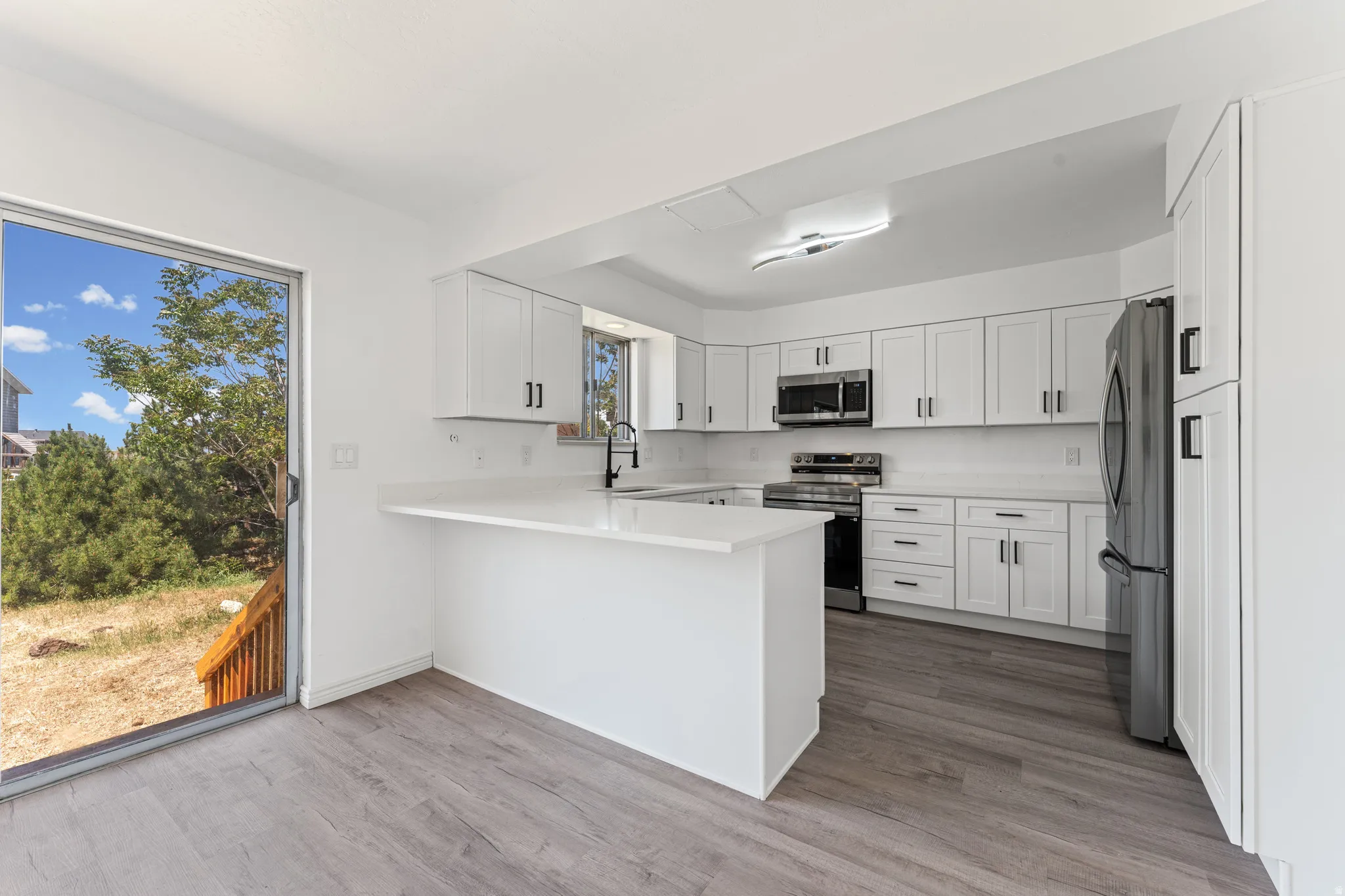 Modern kitchen featuring white shaker cabinetry, stainless steel appliances, a white countertop, and wood-finish flooring