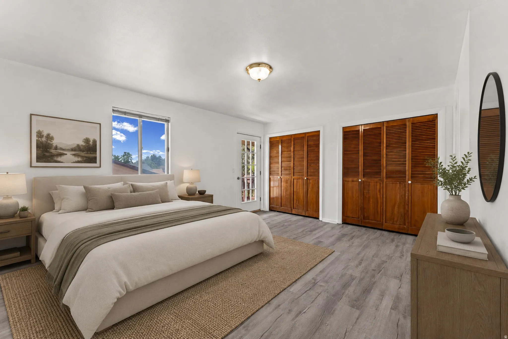 Bright interior space with light wood-finish flooring, featuring two sets of bi-fold louvered closet doors, a large window, and a door with glass panels
