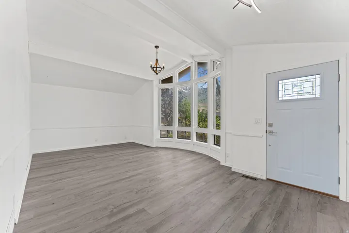 Bright interior space featuring a curved bay window, vaulted ceilings with exposed beams, wood-finish flooring, wainscoting, and a front entry door with decorative glass