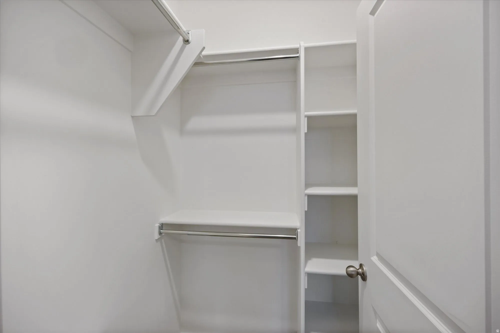 Walk-in closet featuring white built-in shelving, multiple hanging rods, and a white interior door with a brushed nickel knob