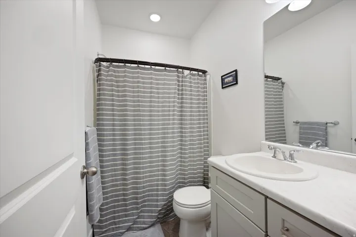 Bathroom featuring a single vanity with an integrated sink, a large mirror, overhead lighting, and a toilet