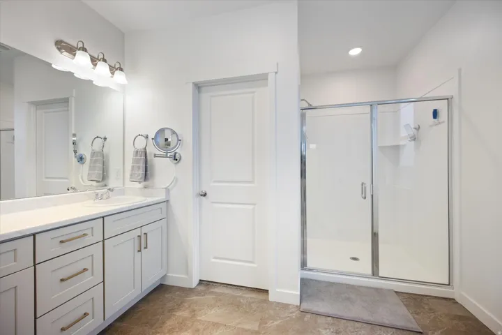 Bathroom featuring a single vanity with light grey cabinetry and gold-tone hardware, a white countertop, and a built-in mirror