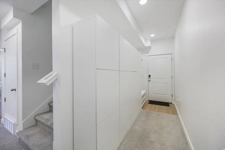 Entryway featuring integrated white cabinetry, recessed lighting, wood-finish flooring, and gray carpeted stairs with a white handrail