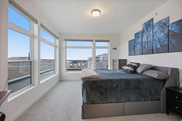 Bright bedroom with floor-to-ceiling windows, light carpeting, and a neutral color palette