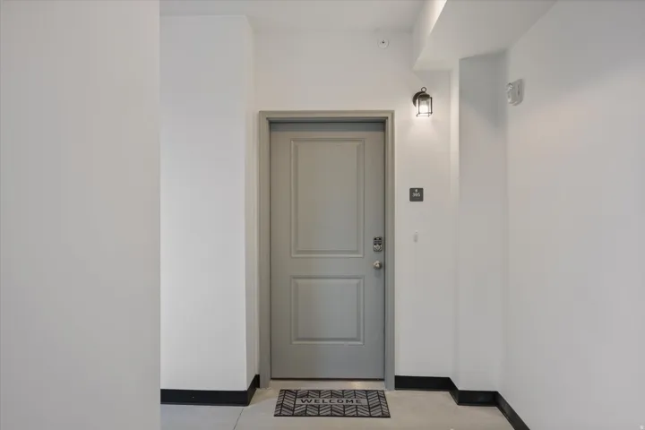 Entry door featuring a panel design, wall-mounted sconce lighting, and a digital keyless entry system