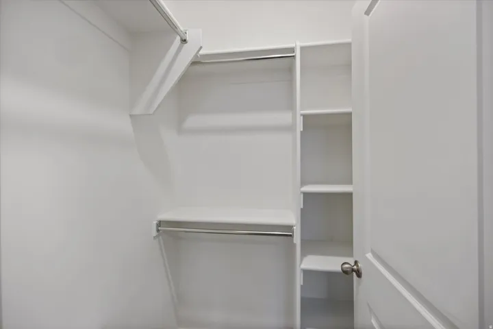 Walk-in closet featuring white built-in shelving, multiple hanging rods, and a white interior door with a brushed nickel knob