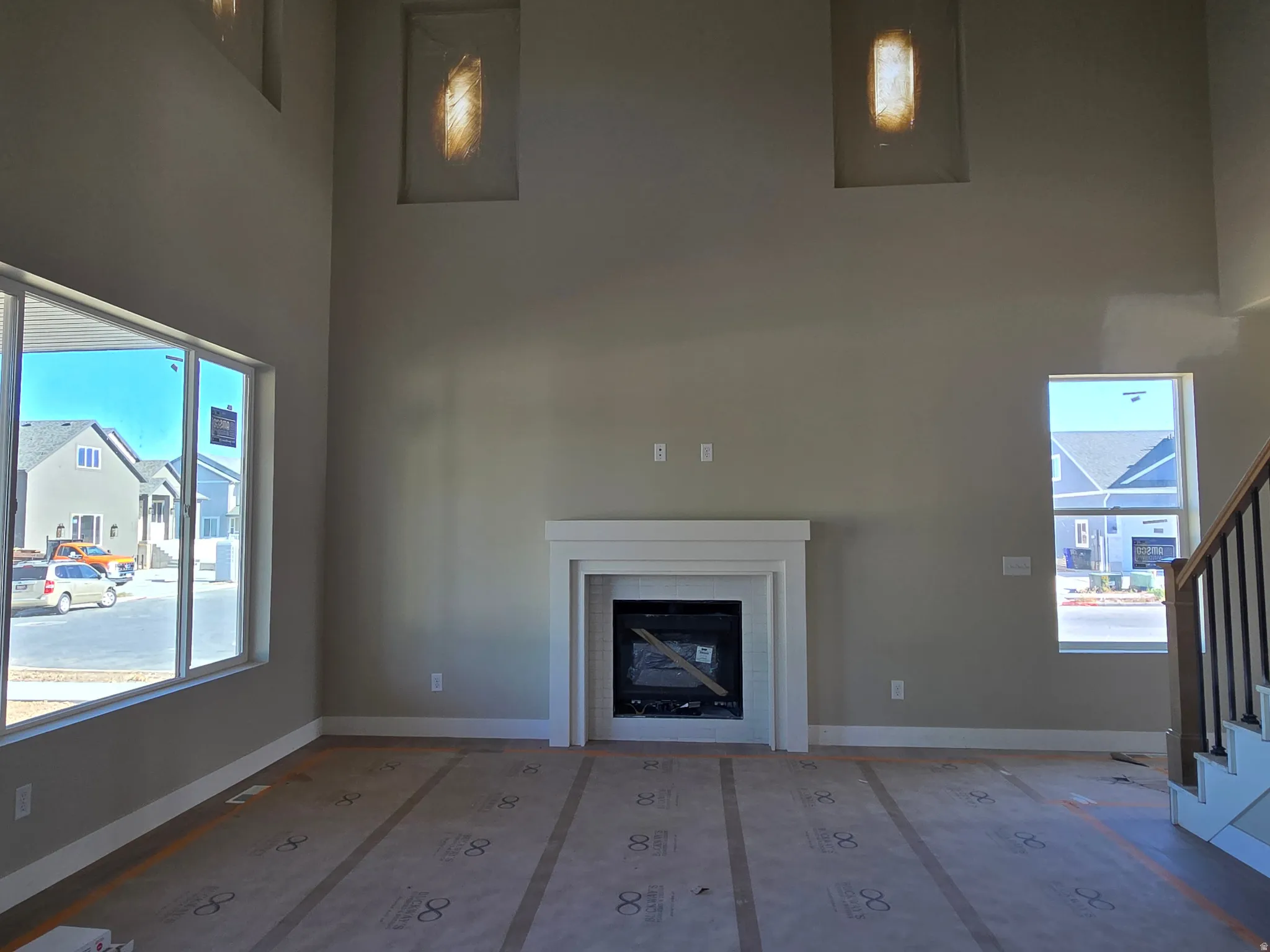 Two-story living area featuring a white mantel fireplace, large windows, recessed wall lighting, and a staircase with wood handrails and black balusters