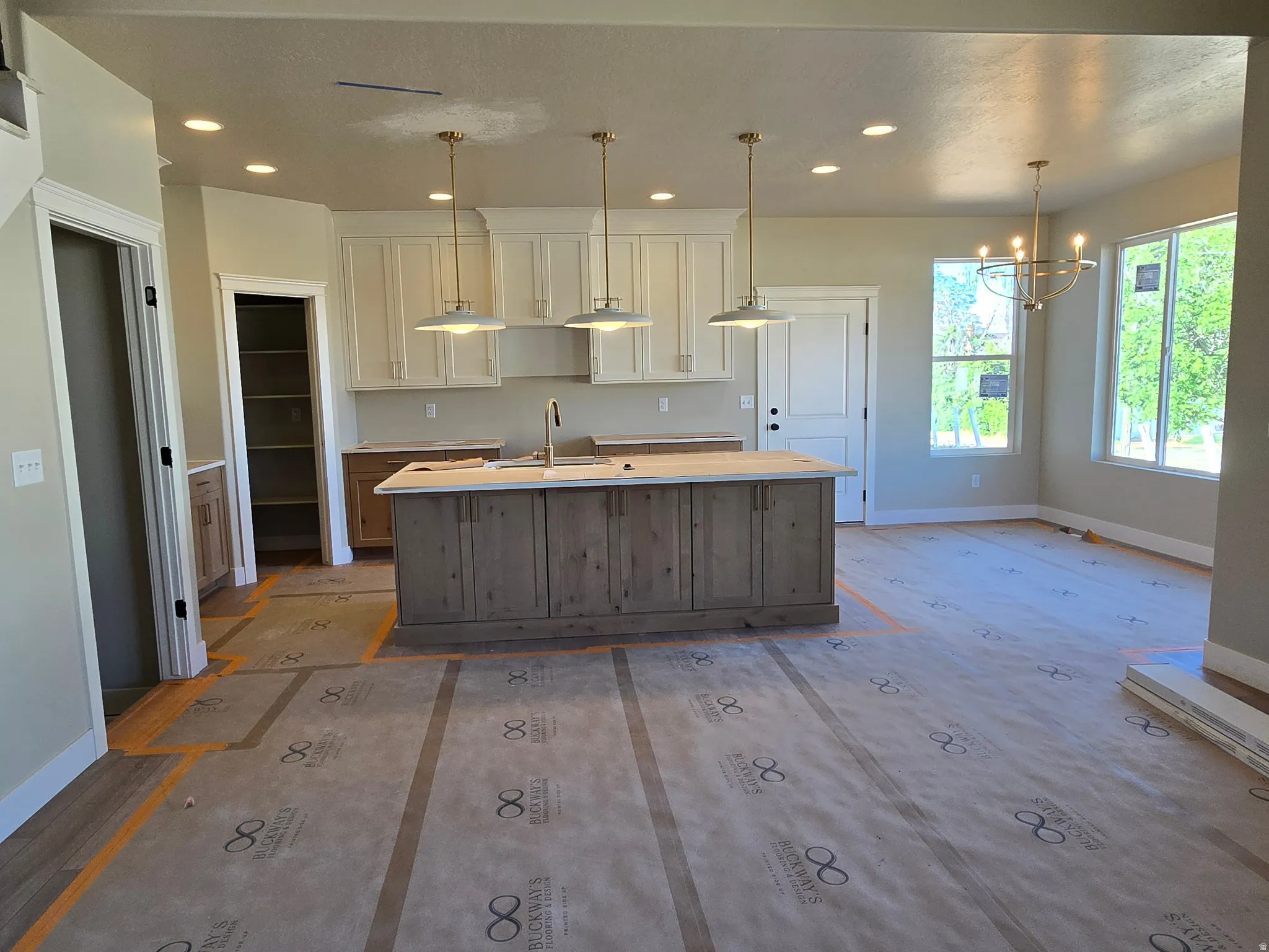 Open-concept kitchen and dining area featuring a spacious island with a single-basin sink and brass faucet, white shaker-style cabinetry, and recessed lighting