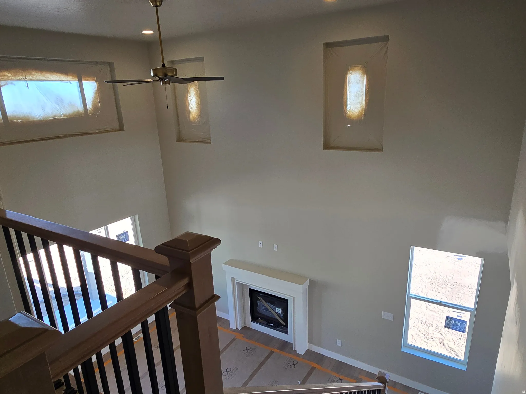 Two-story interior featuring a wood-finish staircase with black balusters, a ceiling fan with integrated lighting, a fireplace with a white mantel, and multiple windows