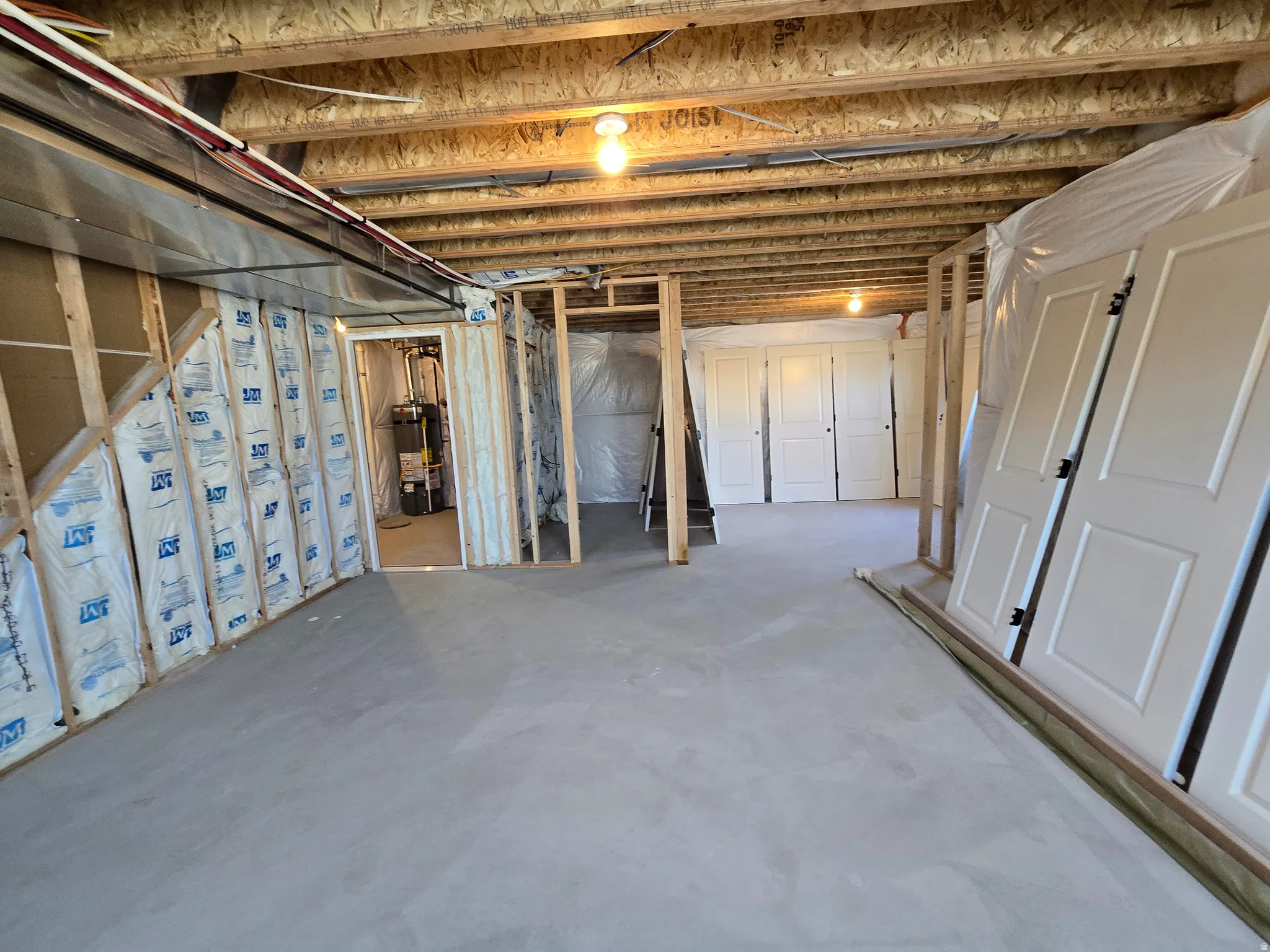 Unfinished basement space featuring exposed wood joists, concrete flooring, framed interior walls, and visible insulation