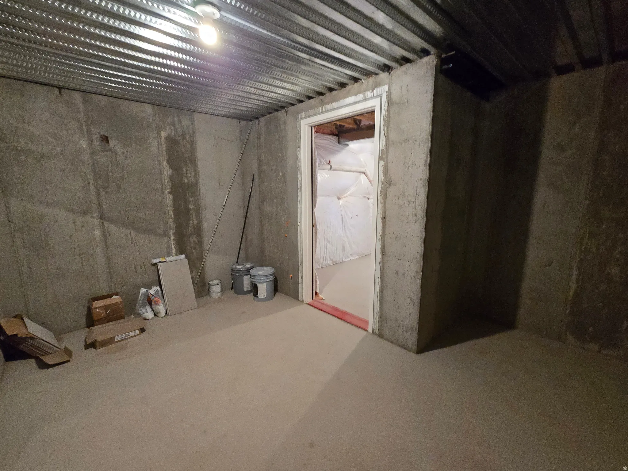 Unfinished concrete room featuring exposed metal joists and a bare bulb light fixture