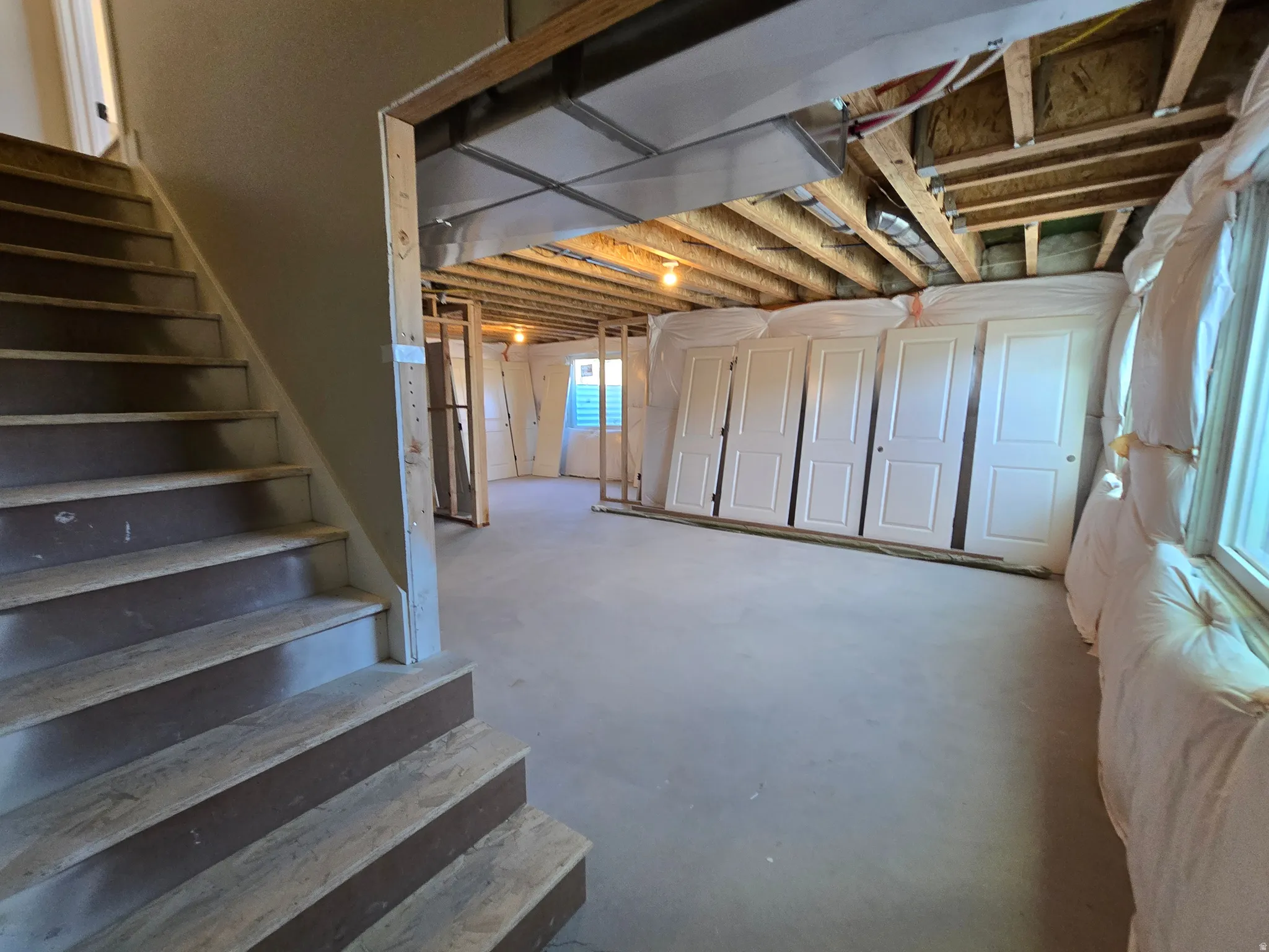 Unfinished lower level featuring exposed ceiling joists, concrete flooring, interior framing, and multiple windows