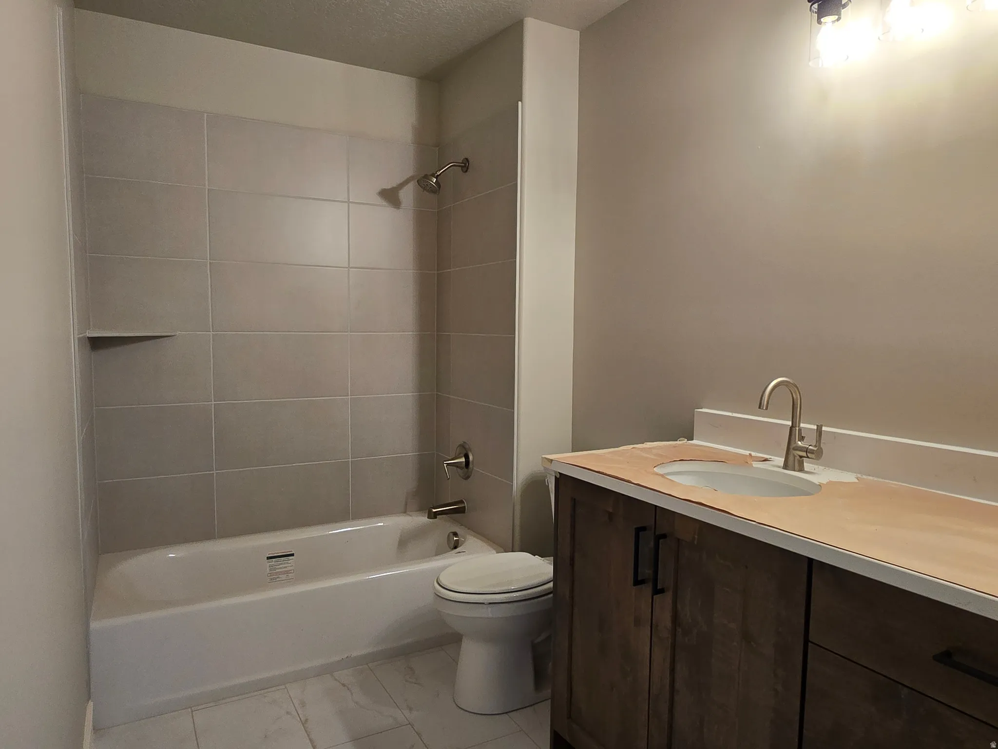 Bathroom featuring a wood-finish vanity with an undermount sink and brushed nickel faucet, a shower/tub combination with light-toned tile surround, and tile flooring