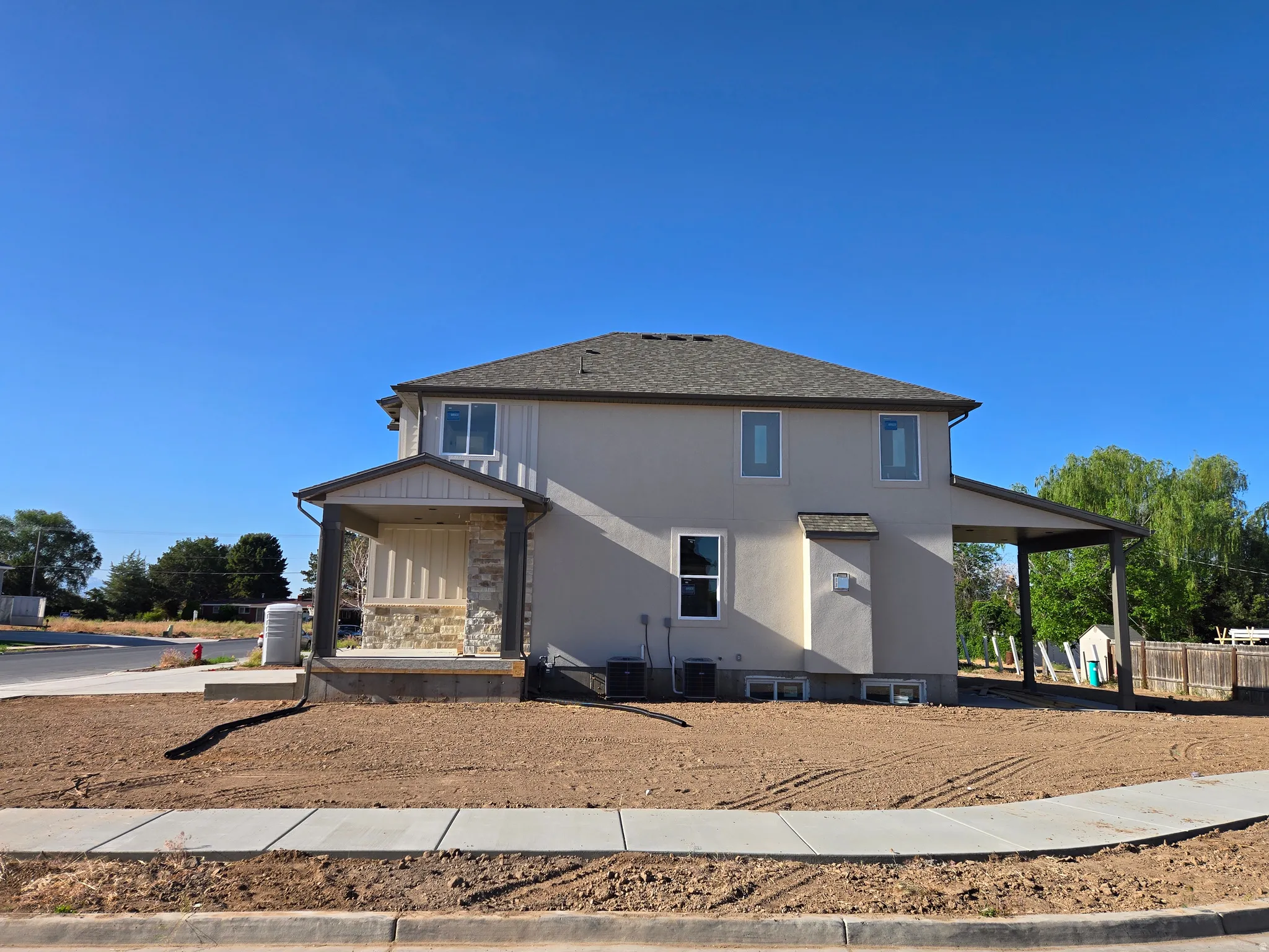 Two-story stucco exterior featuring a covered front porch with stone accents, a covered patio, and a shingle roof