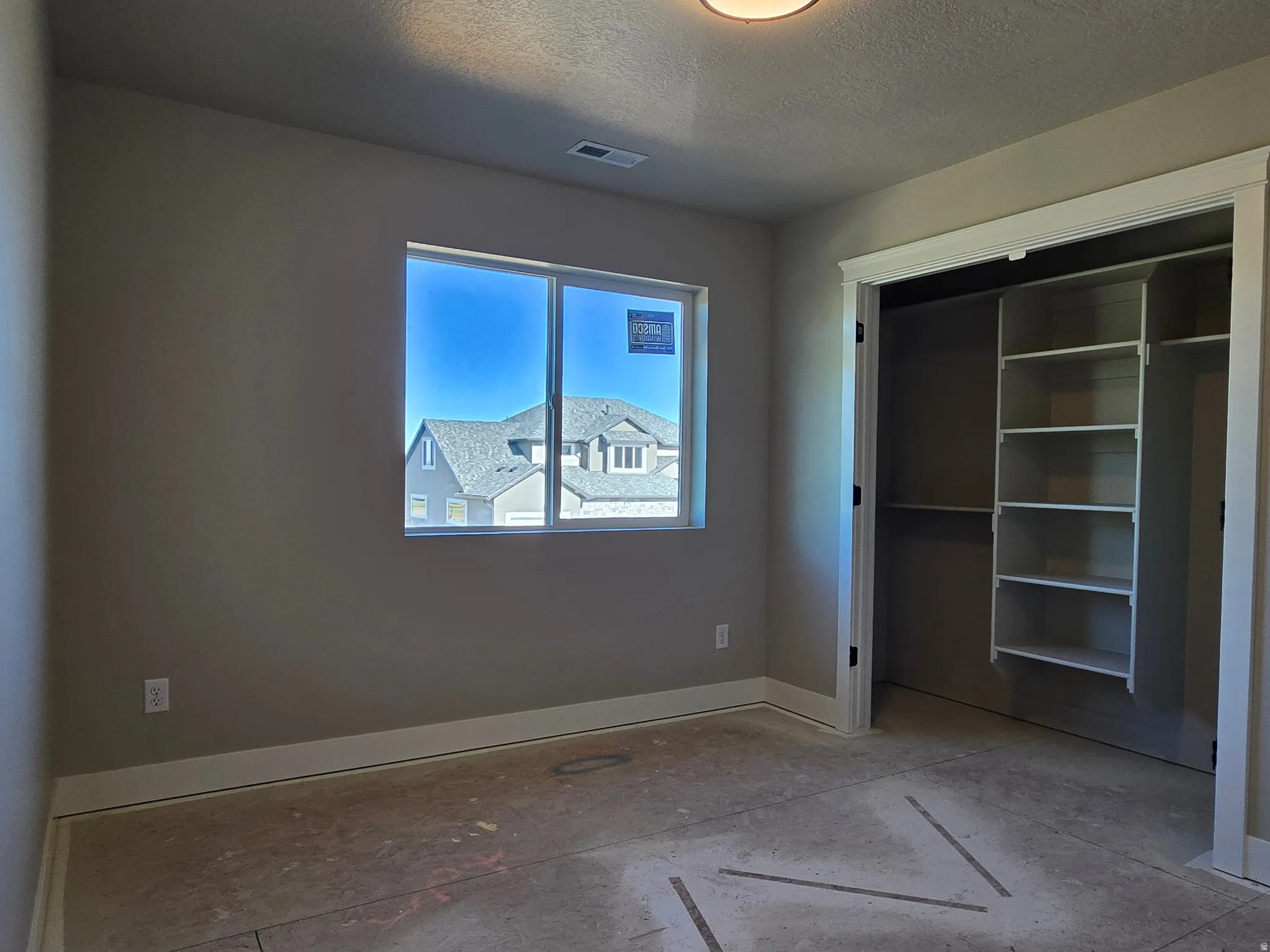 Bedroom featuring a window with a neighborhood backdrop, warm neutral wall paint, white trim, a flush-mount ceiling light, and a closet with built-in shelving