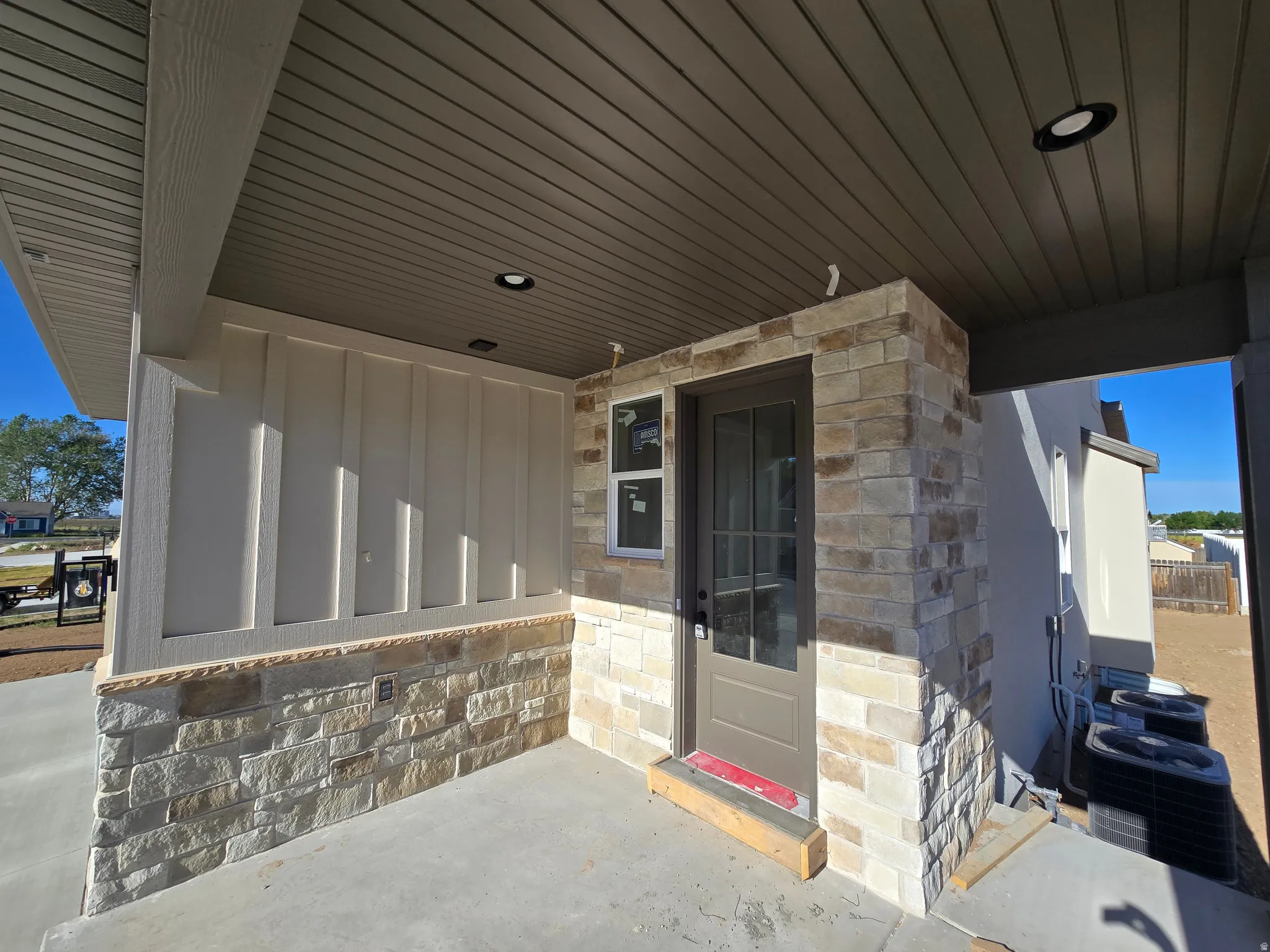 Covered patio featuring a stone veneer accent wall, board and batten siding, recessed lighting, concrete flooring, and a glass-paneled door