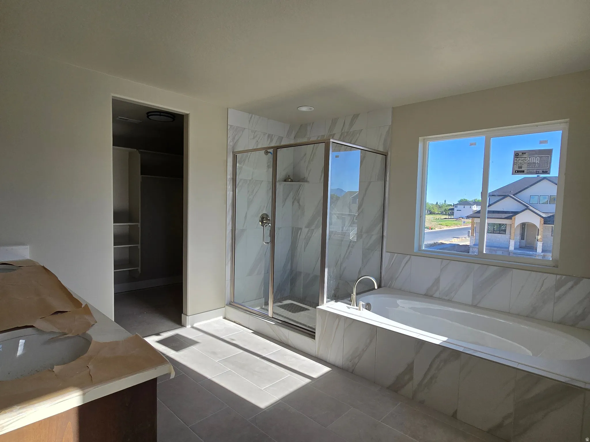 Spacious bathroom featuring a glass-enclosed shower, a large soaking tub with surrounding tile, a double window, and a separate water closet