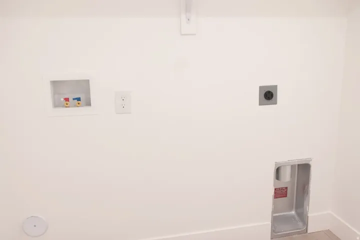 White wall with laundry hookups, including a recessed water supply box, standard electrical outlet, 240V electrical outlet, and dryer vent box