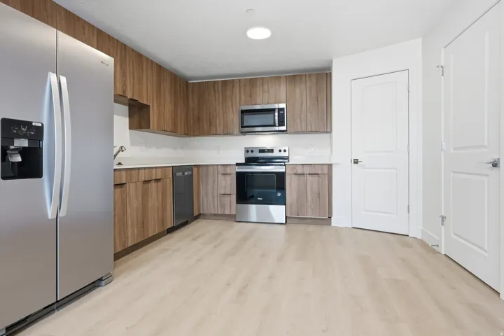 Kitchen featuring wood-finish cabinetry, stainless steel appliances, light countertops, and wood-finish flooring