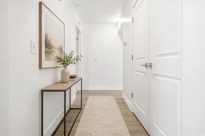 Clean hallway featuring light wood-finish flooring, white walls, and bright overhead lighting. AI decor